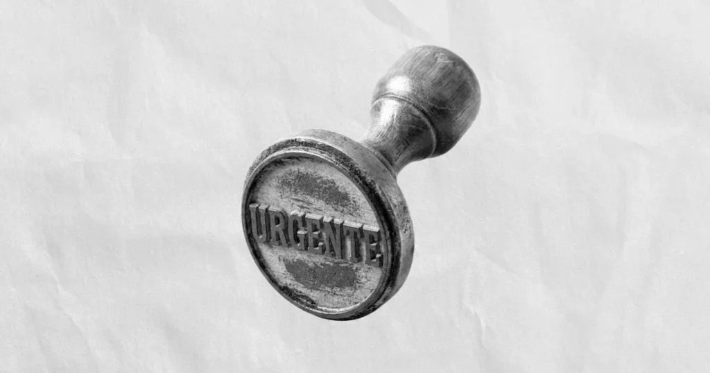 Sello de madera con la inscripción "URGENTE" en primer plano, colocado sobre una textura de papel arrugado.
