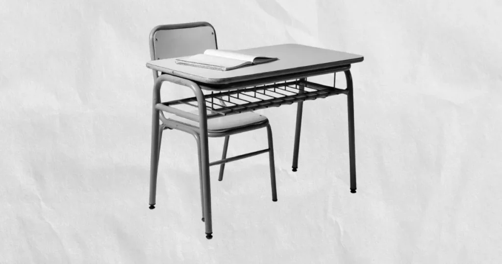 Pupitre escolar vacío con cuaderno abierto en escala de grises sobre fondo de papel arrugado