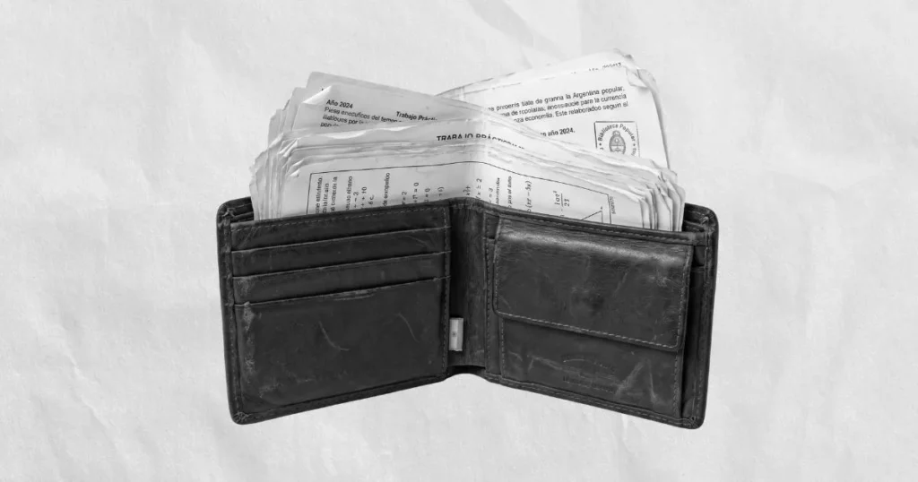 Billetera de cuero abierta en escala de grises sobre fondo de papel arrugado, con fotocopias escolares asomando en lugar de billetes.